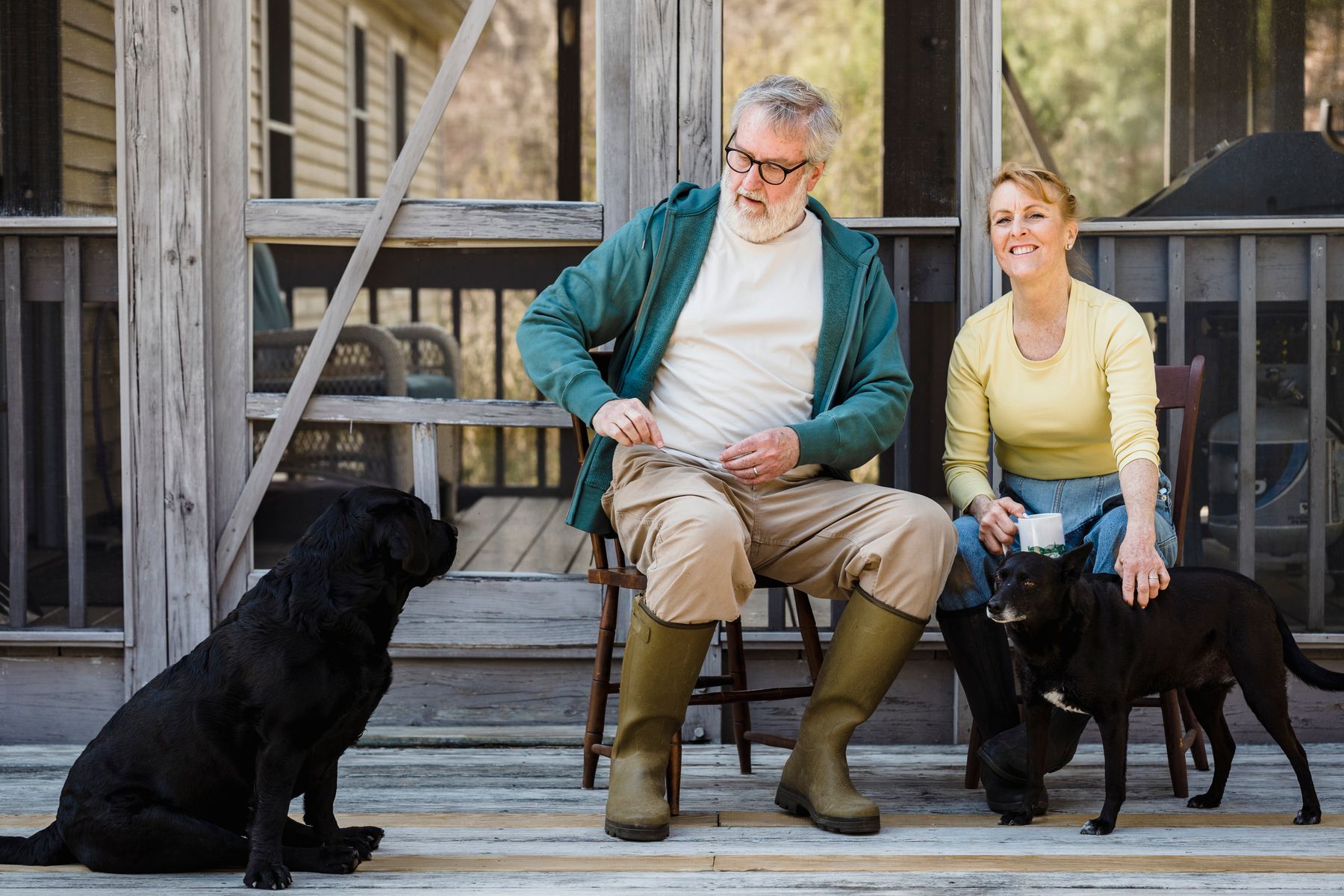 An older couple relaxing together on their front porch with their dogs